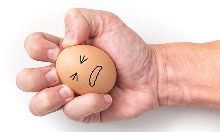 Hand holding a boiled egg with a sad face on it