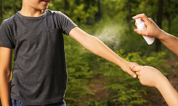 Parent spraying child with bug spray in the woods