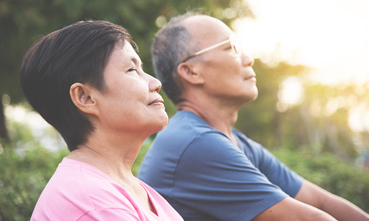 Older couple meditating outdoors in the sunlight