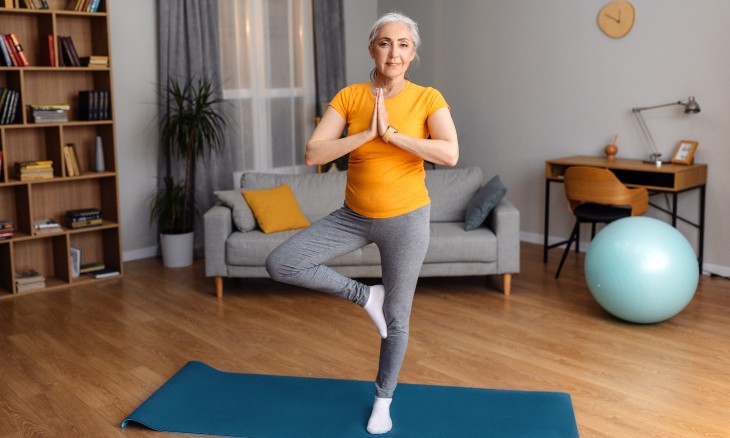 A woman stands in tree pose in her living room.