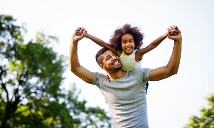 Dad outside holding young daughter on his back with arms outstretched