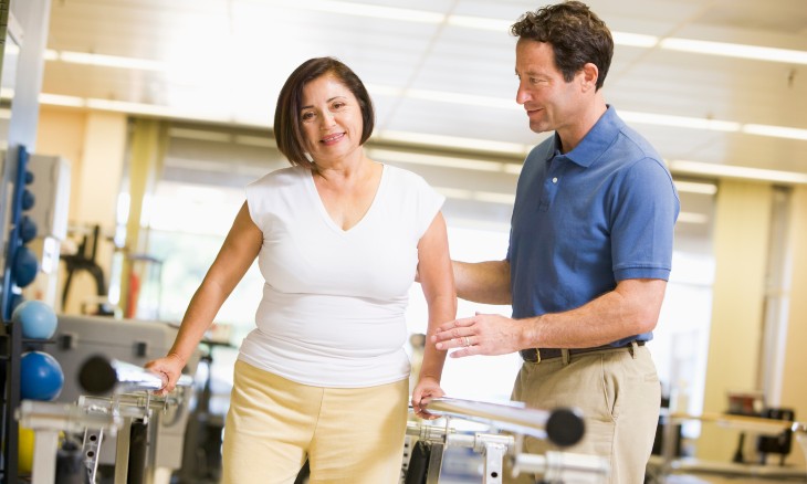 Woman working with physical therapist using parallel bars
