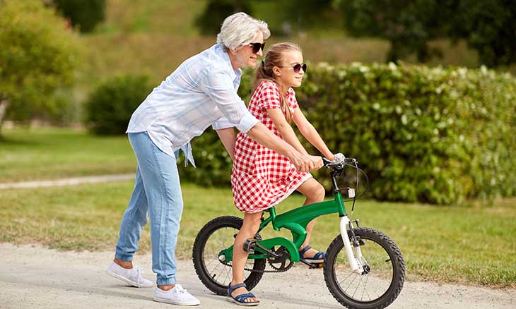 A grandma helps child ride a bike.