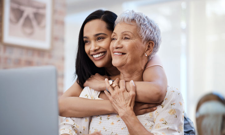 Daughter hugs her mother as they read from laptop.
