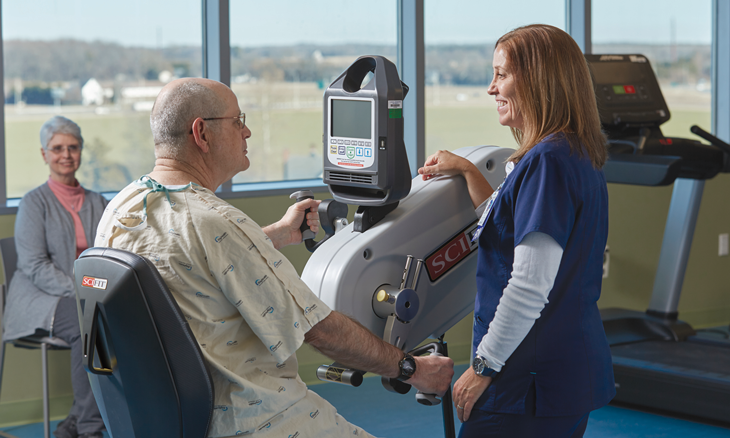 Patient using arm machine with inpatient rehabilitation staff support