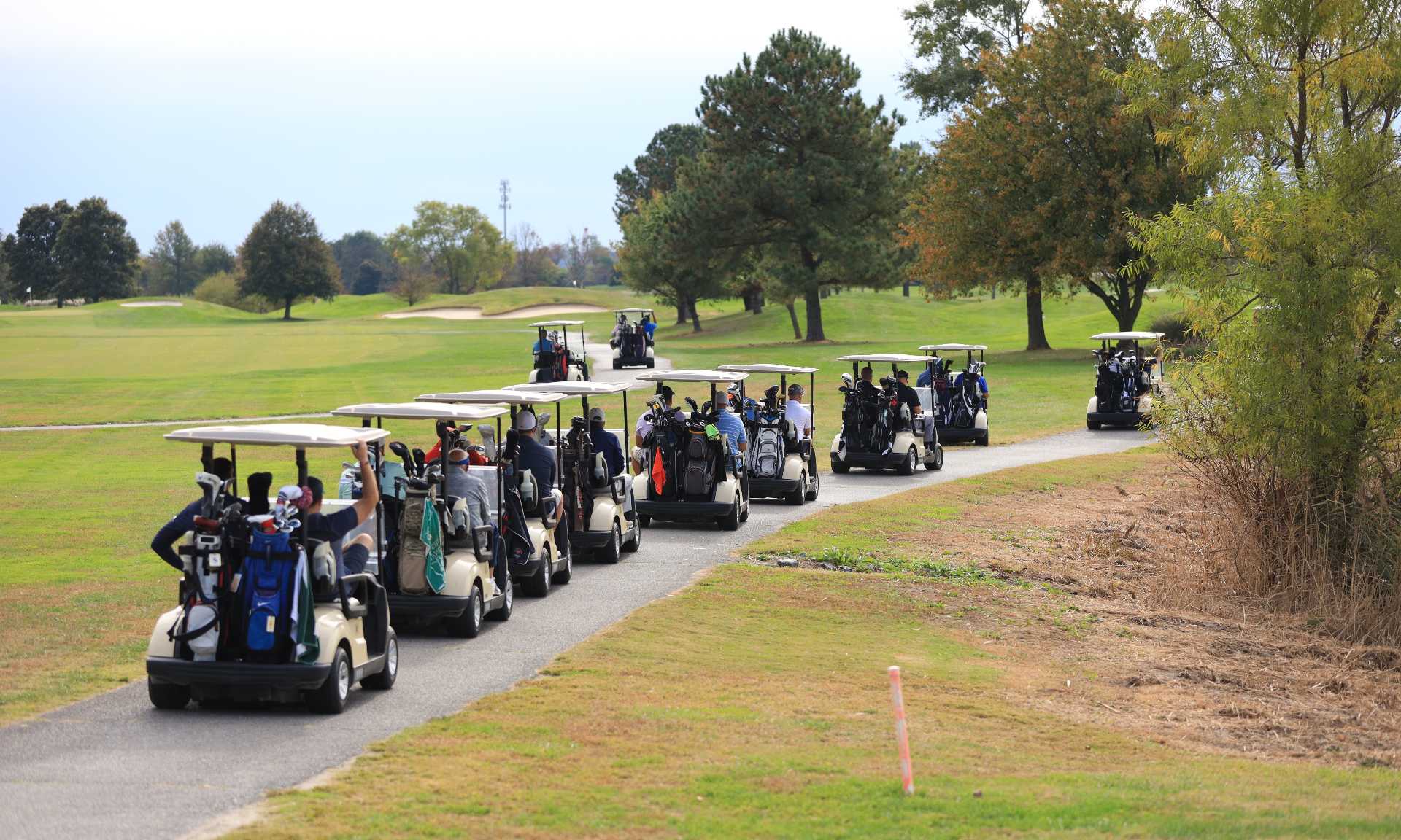 Golf carts filled with golfers participating in tournament drive down path on the golf course.