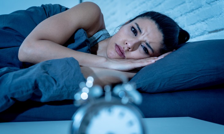 Woman in bed looking frustrated as she stares at the alarm clock during the night