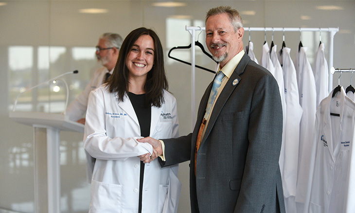 A physician resident is being congratulated by the the residency program director at a White Coat ceremony 