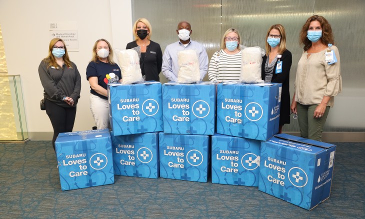 People from a local business and charity stand with Bayhealth representatives behind boxes of blankets and other care items delivered for cancer patients. 