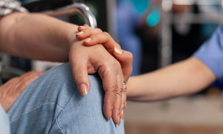 The hand of a healthcare working touching the hand of someone in a wheelchair.