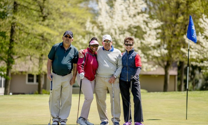 A foursome of golfers pose on the green of a golf course.