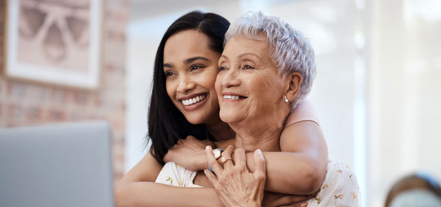 Daughter hugs mom as they read from laptop.