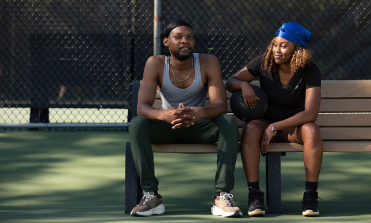 Couple sits on a bench at a basketball court.